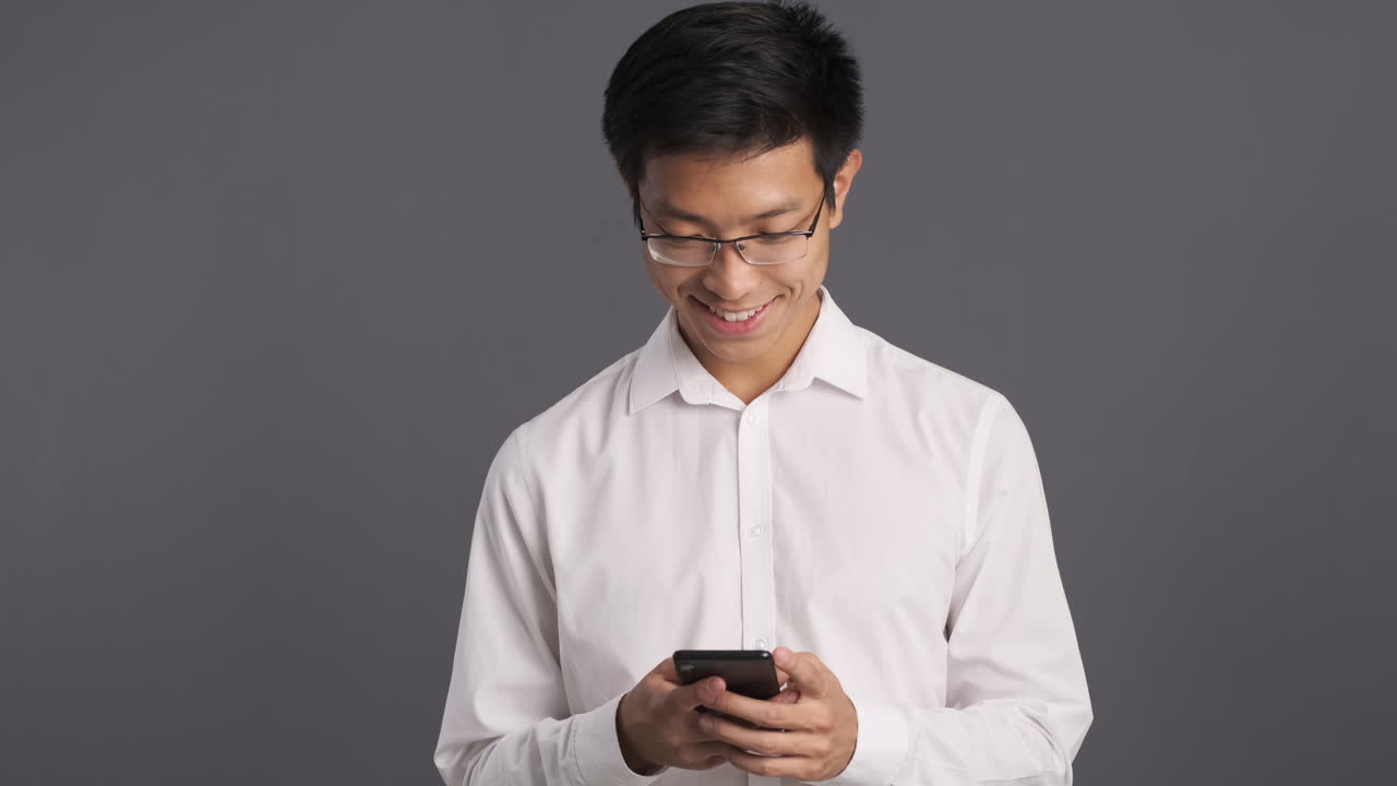 Asian man checking smartphone and smiling.