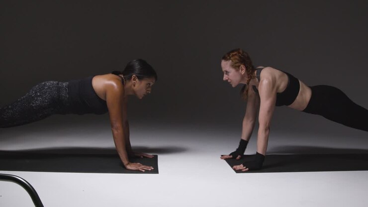 fotografía de estudio de dos mujeres maduras con ropa de gimnasia haciendo ejercicio de tabla juntas