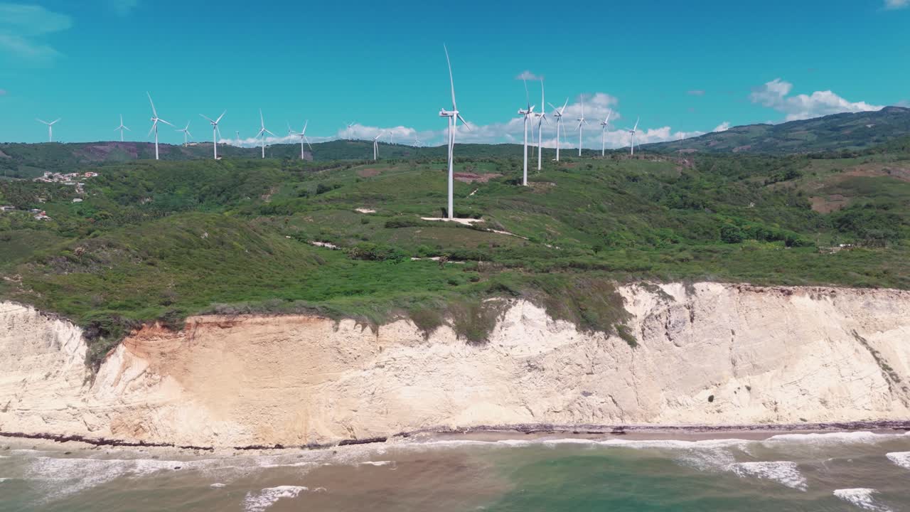 Aerial of wind farm on lush green cliffs above Caribbean Sea, generating sustainable and renewable energy under blue sky, Barahona, Dominican Republic