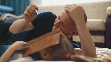 father plays with little daughter hiding face behind book