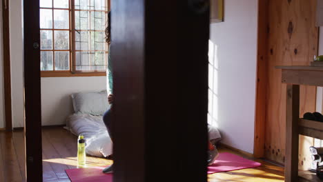 Healthy-mixed-race-woman-exercising,-standing-and-stretching-in-sunny-cottage-bedroom