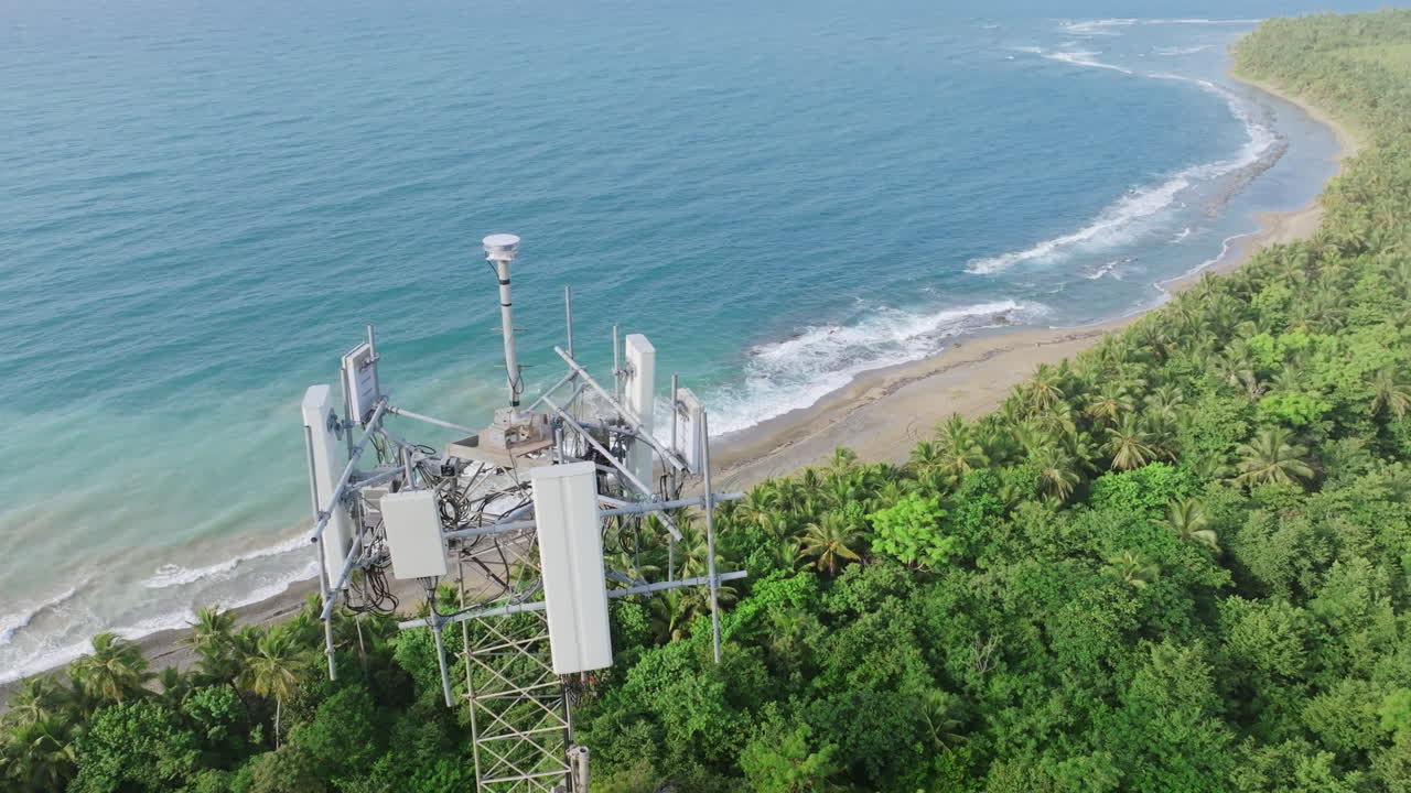 imágenes aéreas panorámicas y moviéndose hacia la cima de una torre de telefonía celular de radio con el océano en el fondo en el sur de puerto rico
