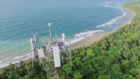 aerial footage panning across and moving towards the top of a radio cell phone tower with the ocean in the background in the south of puerto rico