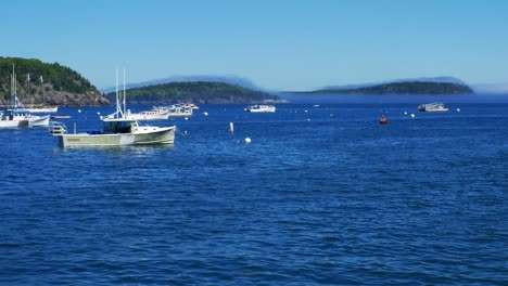 fishing boats moored in blue waters of bar harbor with a light veil of fog sitting on lush green hills in background