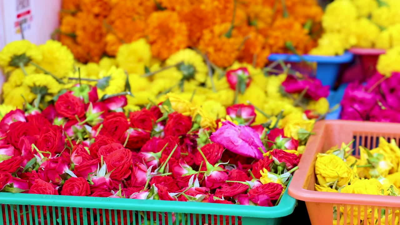 Vibrant trays of fresh flower garlands, including roses and marigolds, displayed at a bustling outdoor market in Singapore. Smooth camera pan, bright natural lighting