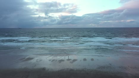 aerial view of a person walking on a beach, dark, gloomy evening, in spain - pan, drone shot