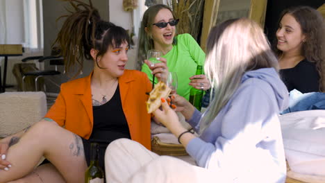 group of four female friends talking and laughing while drinking and eating pizza at home