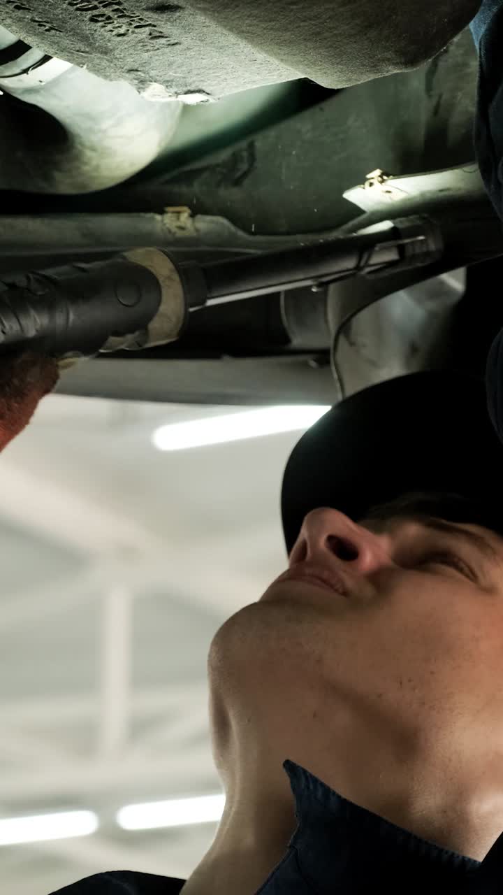 Mechanic Inspecting Car Underside with Flashlight in Auto Repair Shop