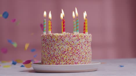 studio shot of paper confetti falling on birthday cake covered with decorations and lit candles being blown out