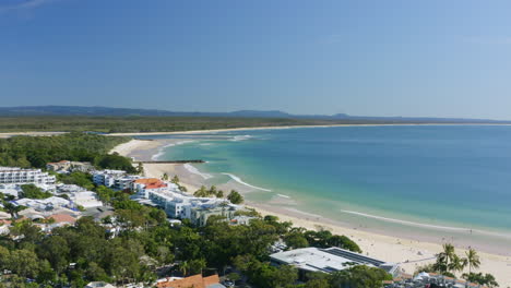 la escénica noosa encabeza la playa principal con la ciudad junto a la playa y vistas al océano azul, dron aéreo de 4k, australia