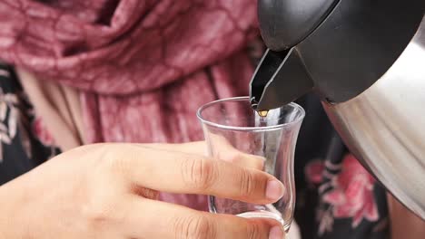 woman pouring tea from a kettle into a glass