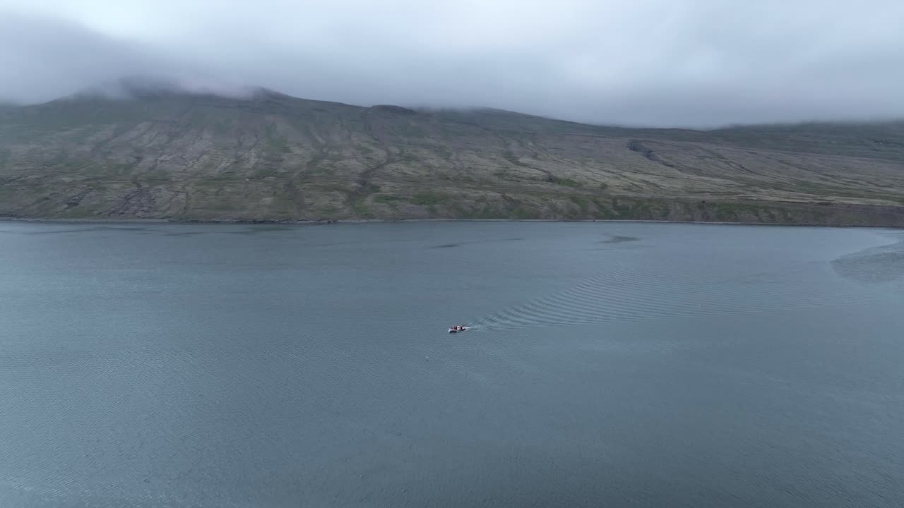 vista aérea sobre un pequeño barco de pesca que viaja en el fiordo faskrudsfjordur en el este de islandia - disparo de drones