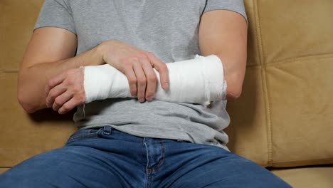 man touches injured arm in gypsum band and sighs tiredly