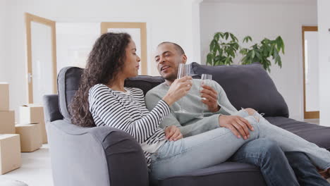 Couple-Taking-A-Break-And-Sitting-On-Sofa-Celebrating-Moving-Into-New-Home-With-Champagne