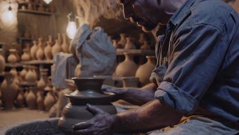 potter shaping clay on a spinning wheel in a workshop filled with finished earthenware vases in avanos, turkey, highlighting the ancient art of pottery making