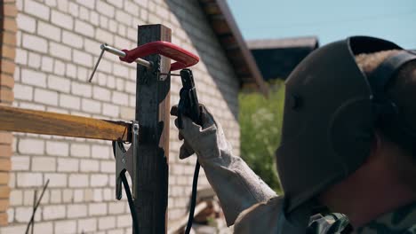 backside-view-man-in-mask-welds-small-detail-to-fence-top