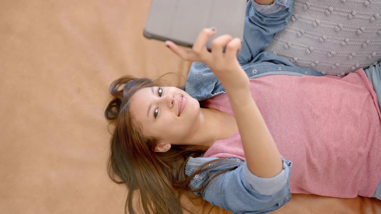 Teen girl adjusting tablet on couch, browsing tech UI icons, binary stream forming social network