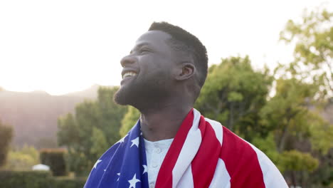 happy african american man standing with flag on back and smiling in sunny garden