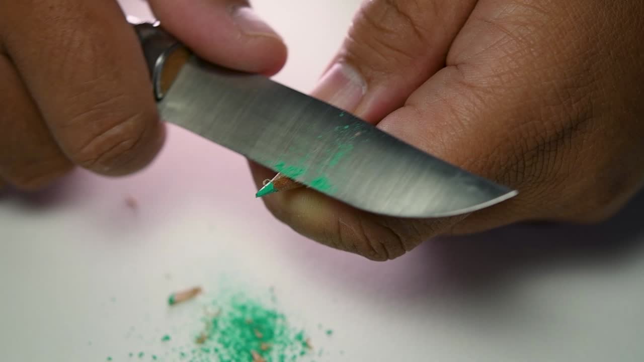 날카로운 칼로 연필과 색연필을 천천히 갈고 있는 손의 영상