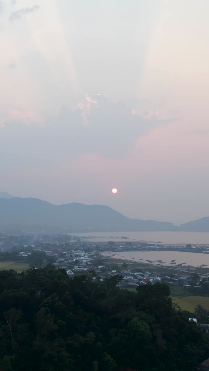 Sunset over a coastal town with mountains and haze