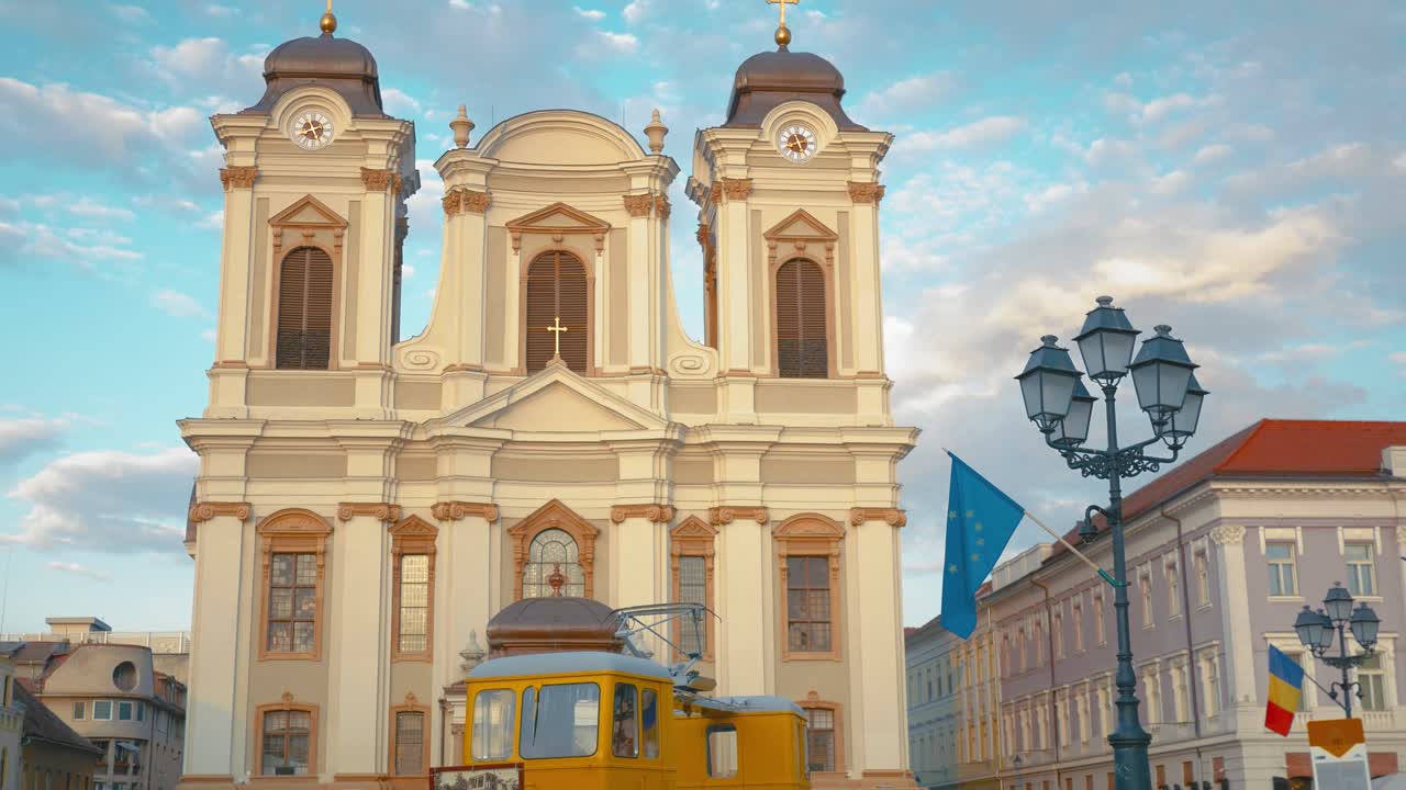 Static shot of Saint George Cathedral, an emblematic baroque-style building in Timisoara, Romania. A yellow old tram and an old street lamp in the foreground