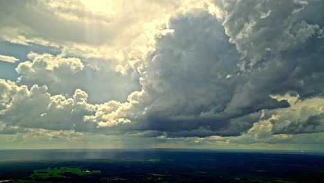 Dramatic-cloudscape-forming-over-lush-green-fields-on-a-bright-sunny-day,-timelapse