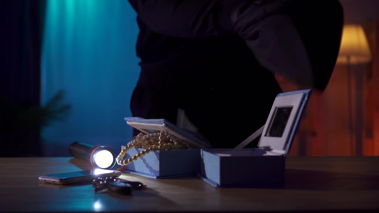 un ladrón con una balaclava roba joyas y dinero de una mesa en la casa