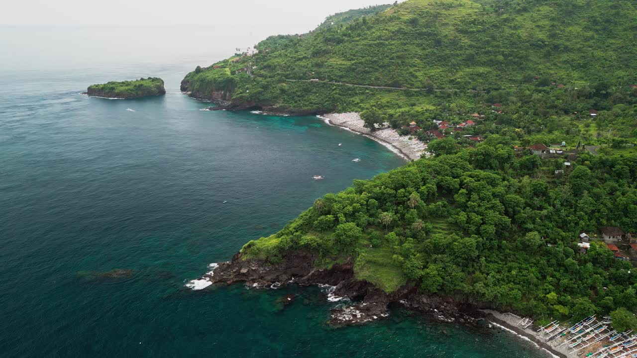 Riprese aeree con drone di tradizionali barche da pesca indonesiane disposte su una piccola spiaggia rocciosa con acqua turchese in una baia tropicale protetta, con un faro distante e un piccolo isolotto panoramico.