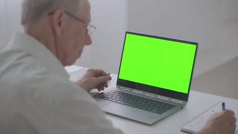 elderly person is learning online, using laptop, green screen for chroma key technology, distant education