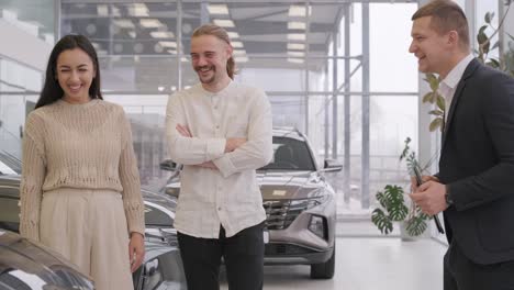 young car salesman showing to young couple new automobile at dealership salon.