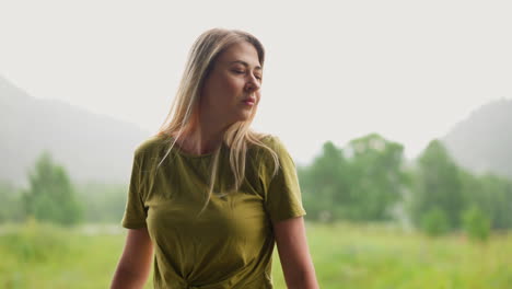 mujer pensativa con el cabello suelto cerca del campo contra la montaña