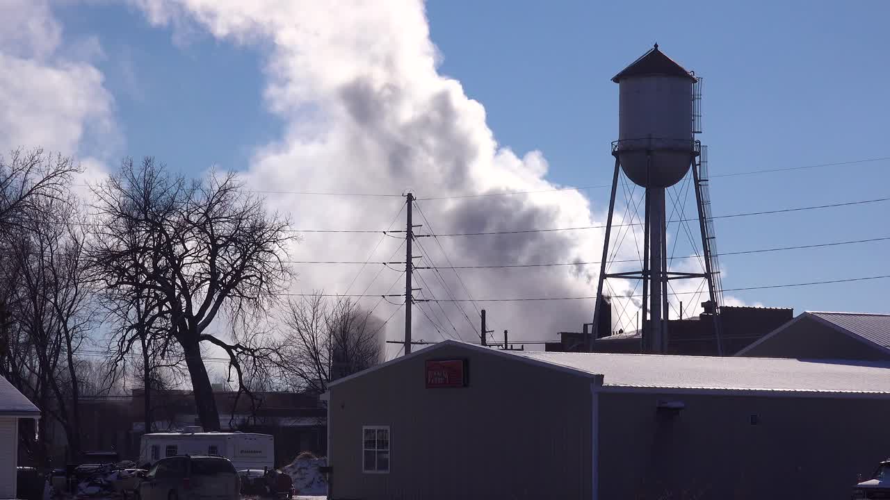 In an industrial town factory smoke pours forth from behind a water tower