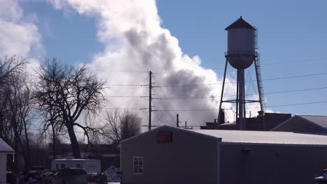 in an industrial town factory smoke pours forth from behind a water tower