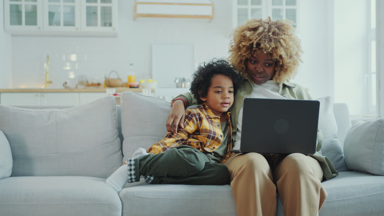 Black Mother Hugging Little Son and Discussing Something on Laptop at Home
