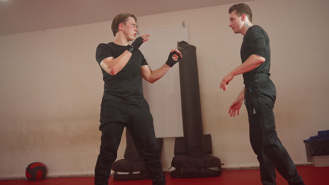Boxer practicing martial arts sparring with partner in gym, wearing black sportswear, engaged in dynamic training with defensive posture and active movement, showcasing combat skills, coordination