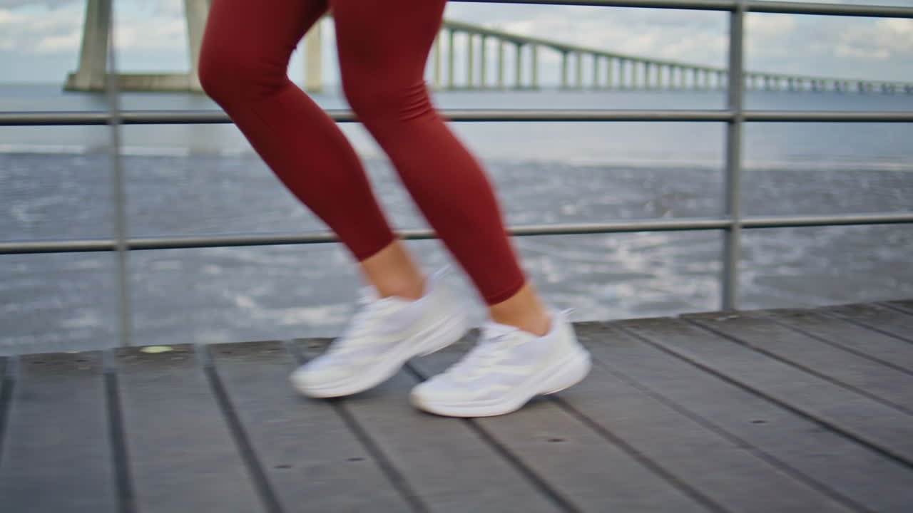 Closeup slim legs running wooden pier on coast. Energetic runner training beach