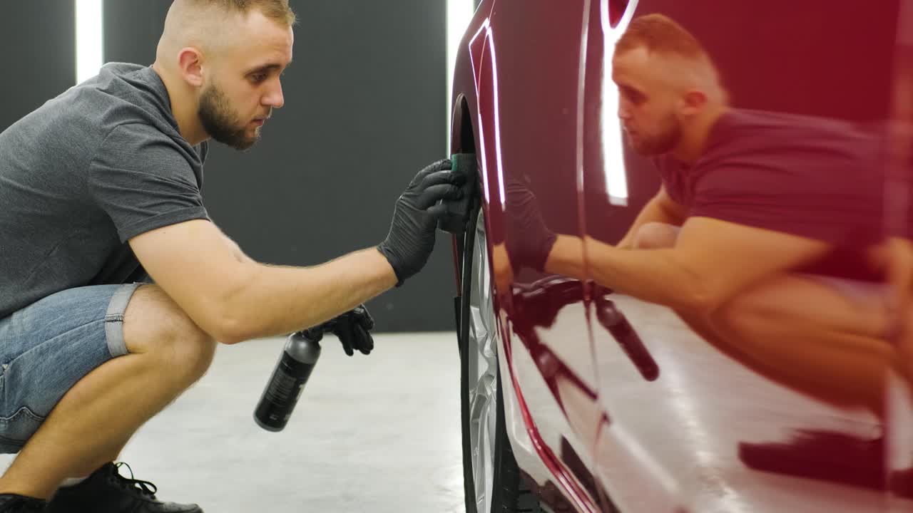 남자 노동자 가 자동차 세탁소 에서 자동차 의 합금 바 를 고 있다