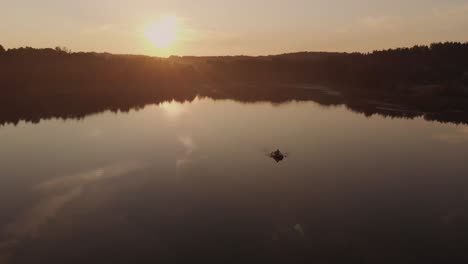 lone man paddling a boat in the middle of a quiet lake in the village near rogowko, poland through golden hour