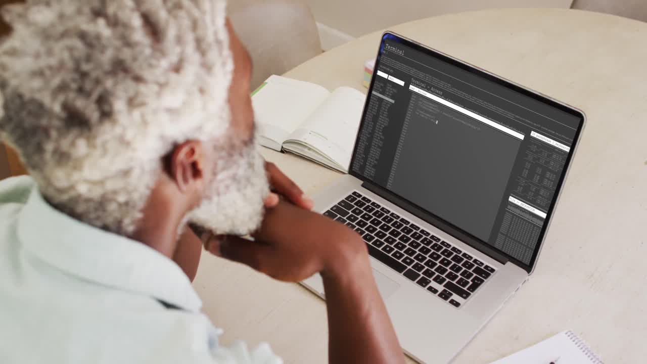 African american man sitting at desk watching coding data processing on laptop screen