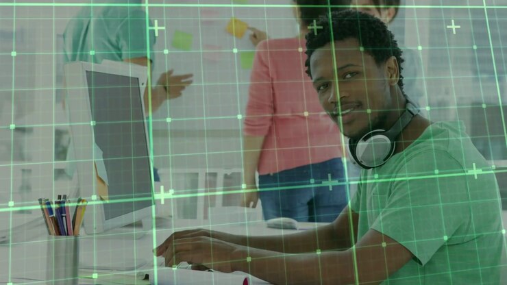 Typing man in green tee with headset working at PC, team arranging sticky notes for planning