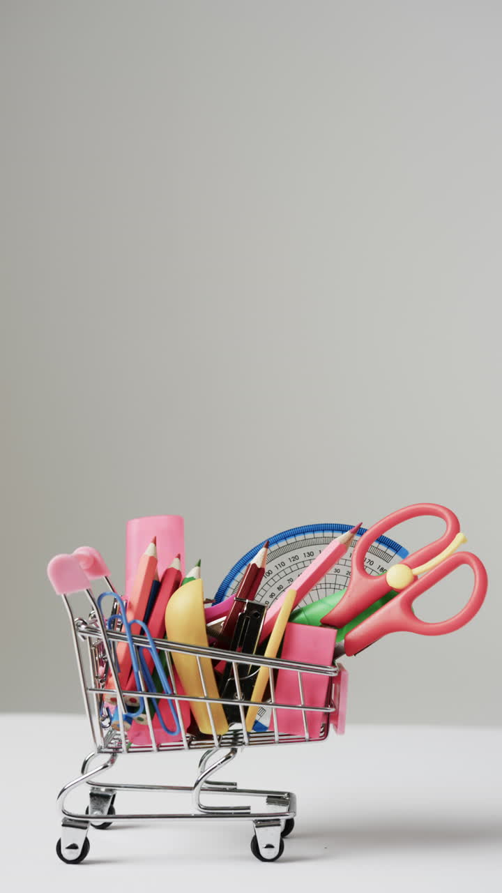 Vertical video of close up of shopping trolley with school items and copy space on grey background