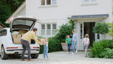 família do lado de fora da nova casa no dia da mudança descarregando caixas do carro