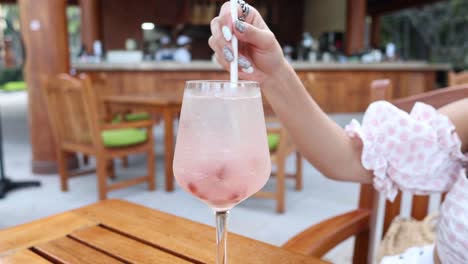 stirring a fizzy pink beverage in a glass