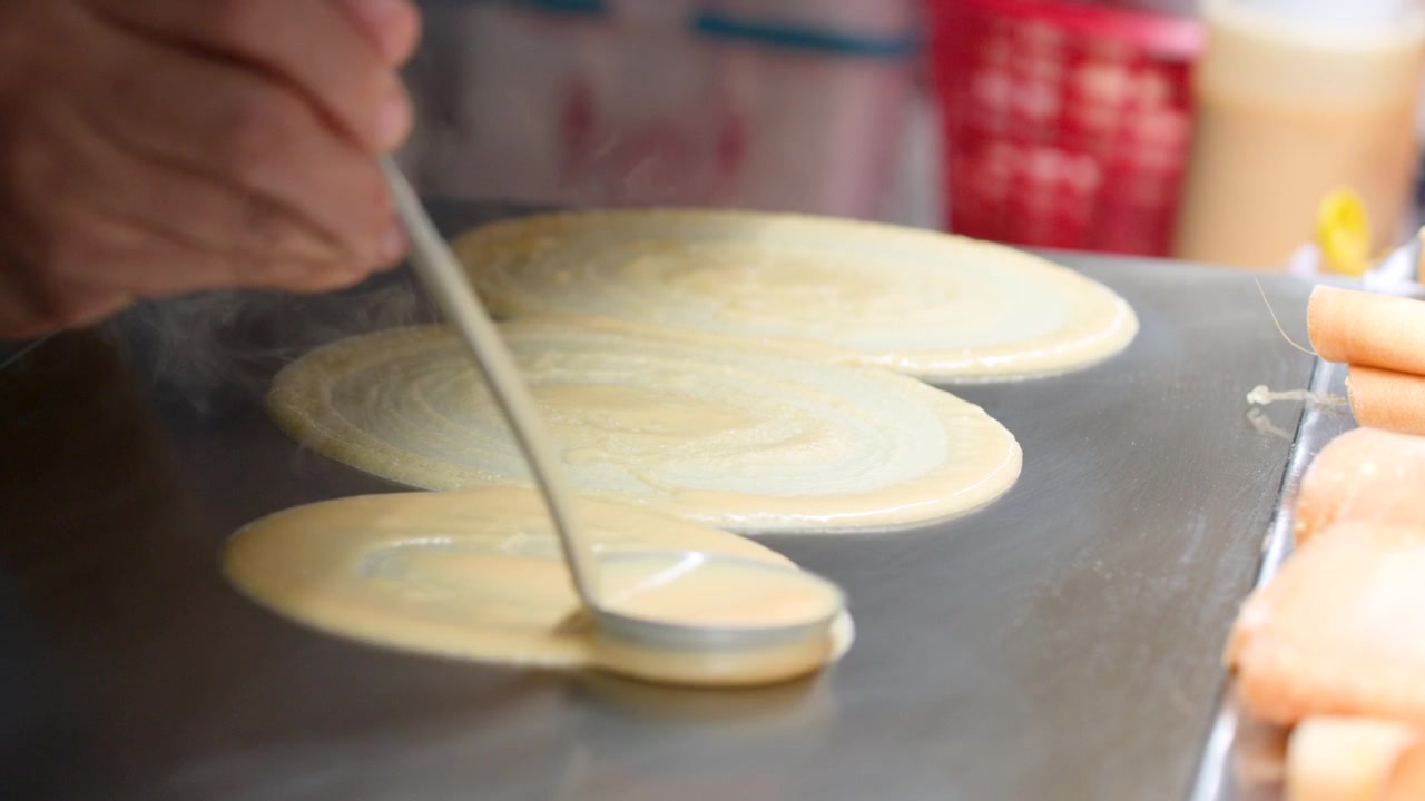 Close-up shot of a vendor using a ladle to spread pancake batter on a griddle.
