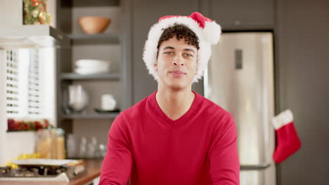 biracial man wearing christmas hat on video call in kitchen at home, slow motion, copy space