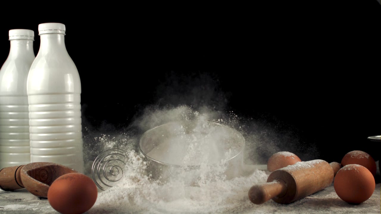 Farina setacciata al rallentatore con ingredienti da forno su sfondo nero