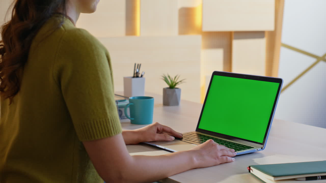 Woman working on a laptop with green screen on desk