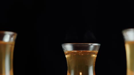three glasses with steaming golden liquid on black background