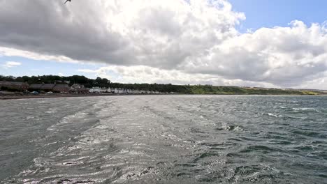 wide-angle daytime shot pans slowly across cromarty’s waterfront, capturing choppy water, historic seaside houses, dramatic clouds, and natural coastal scenery