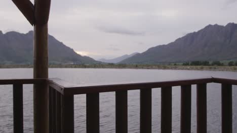 a view of a lake and mountains during sunset on a cloudy day seen from log cabin window